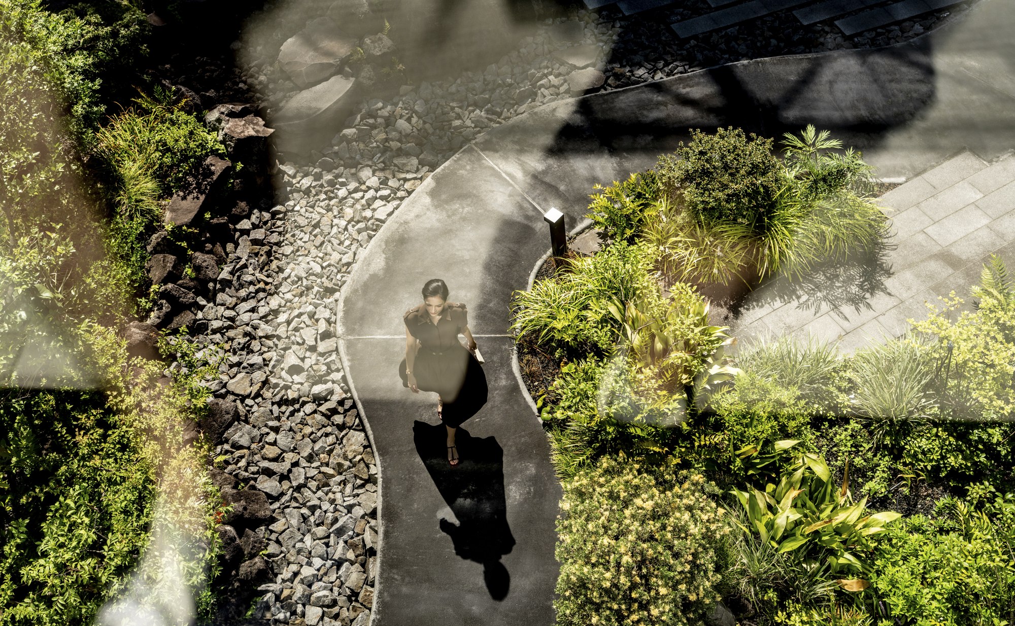 A woman walks through a landscaped hotel courtyard, seen from above through a curved glass reflection.