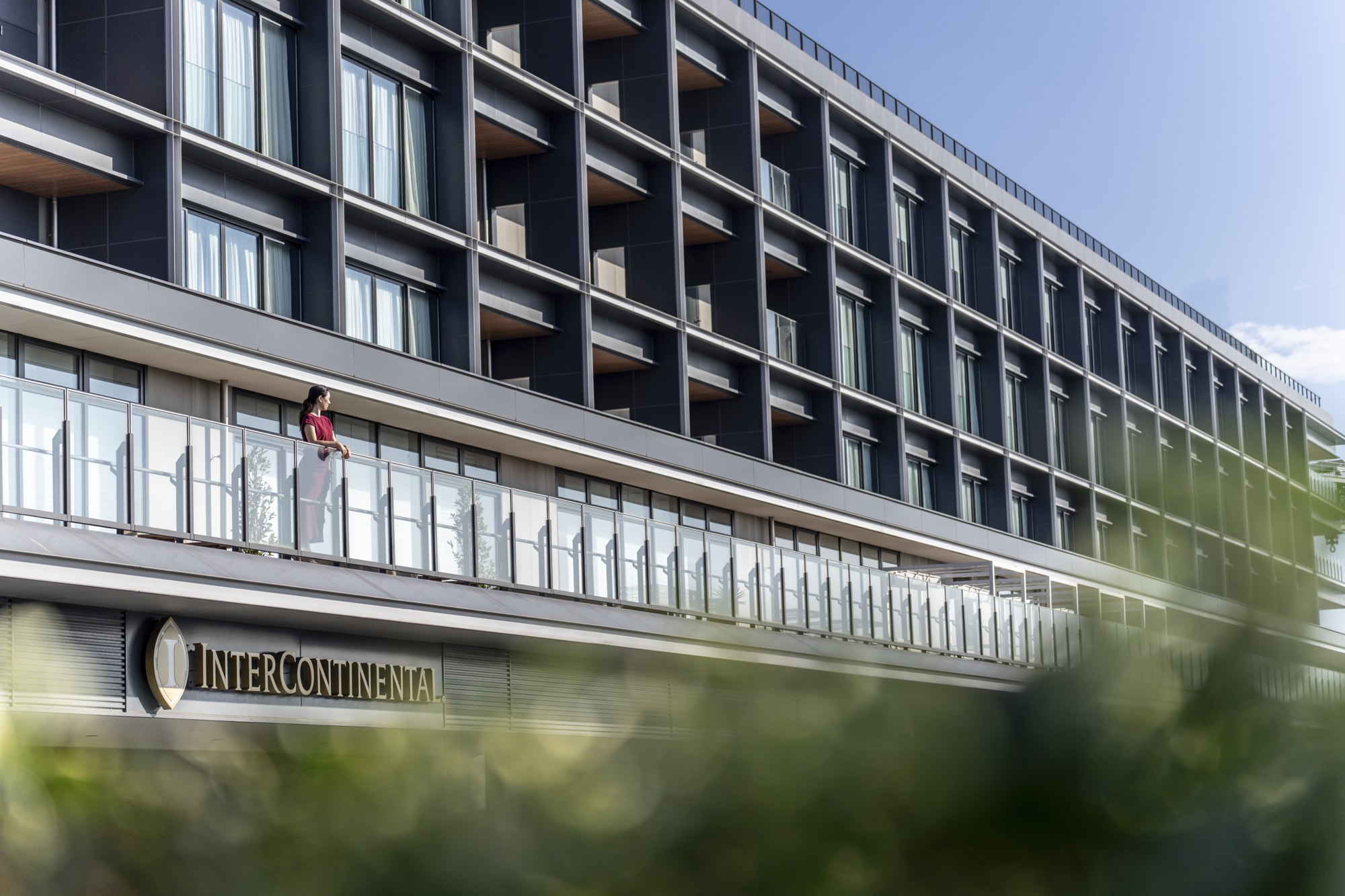 A woman in red stands on a balcony along the exterior of InterContinental Yokohama Pier 8 in Japan.