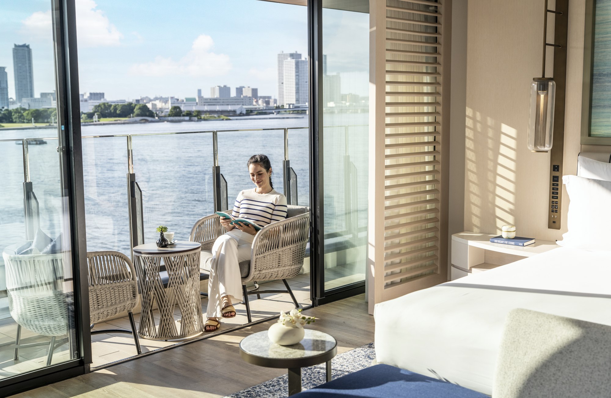 A guest relaxes on a waterfront balcony viewed from inside a hotel room at InterContinental Yokohama Pier 8.