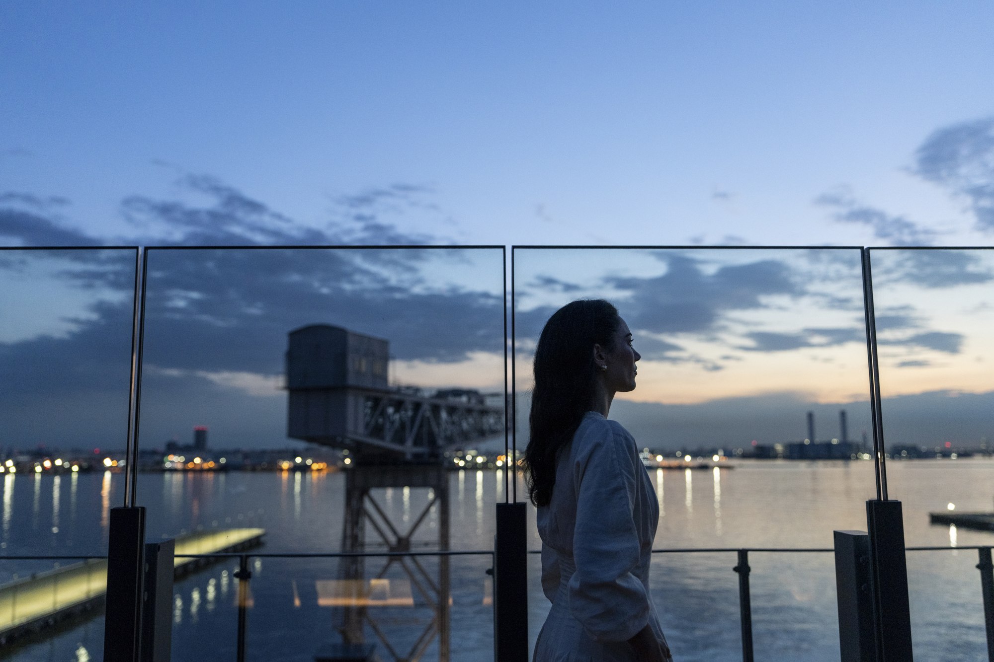 A solo traveler looks across Yokohama harbor from the hotel rooftop at dusk.